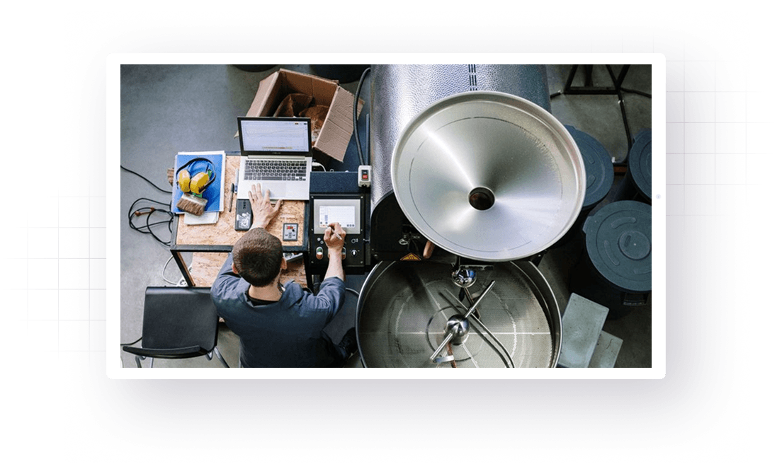 Dynamics 365 ERP for food and beverage manufacturing: operator logging a roasting batch on a laptop beside the roaster